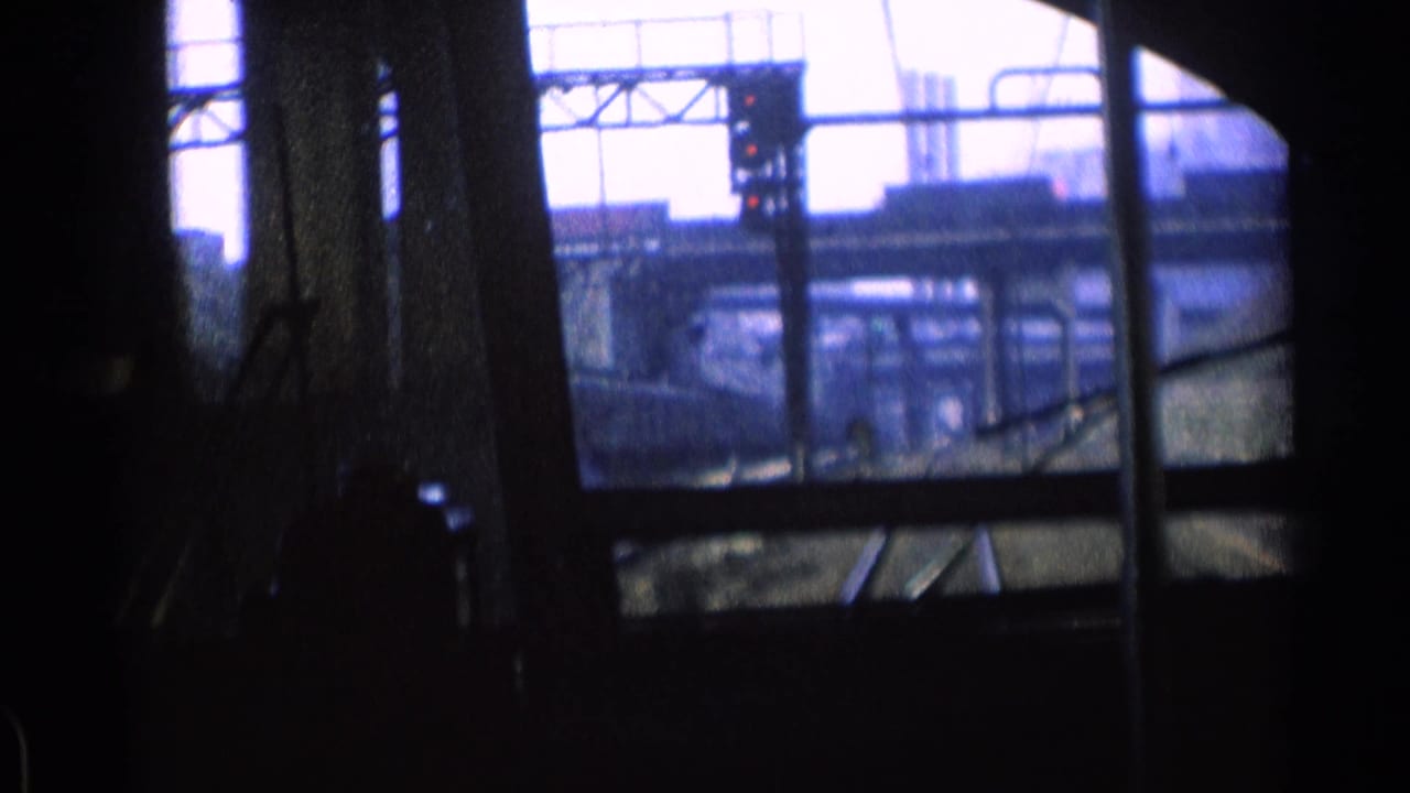 From inside a moving train in Chicago in 1976, dark window framing surrounds tracks, steel supports, and industrial rail structures.