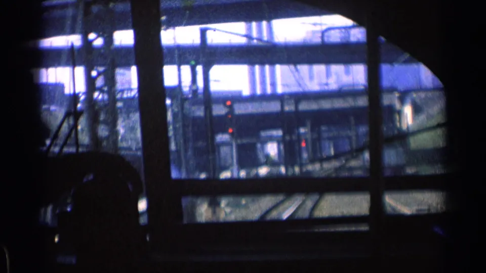 A blue-tinted 1976 Chicago train-window view shows rails, signal lights, and industrial structures behind silhouetted interior elements.