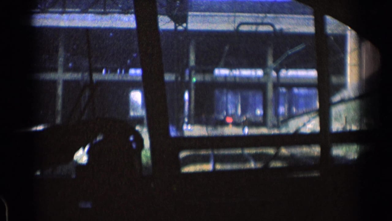 Dark train window view of adjacent rail structure and lit platform areas.
