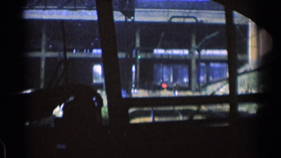 1976 Chicago 8mm frame looking through a dark train or trolley window toward tracks, railings, and lit concrete transit structures.