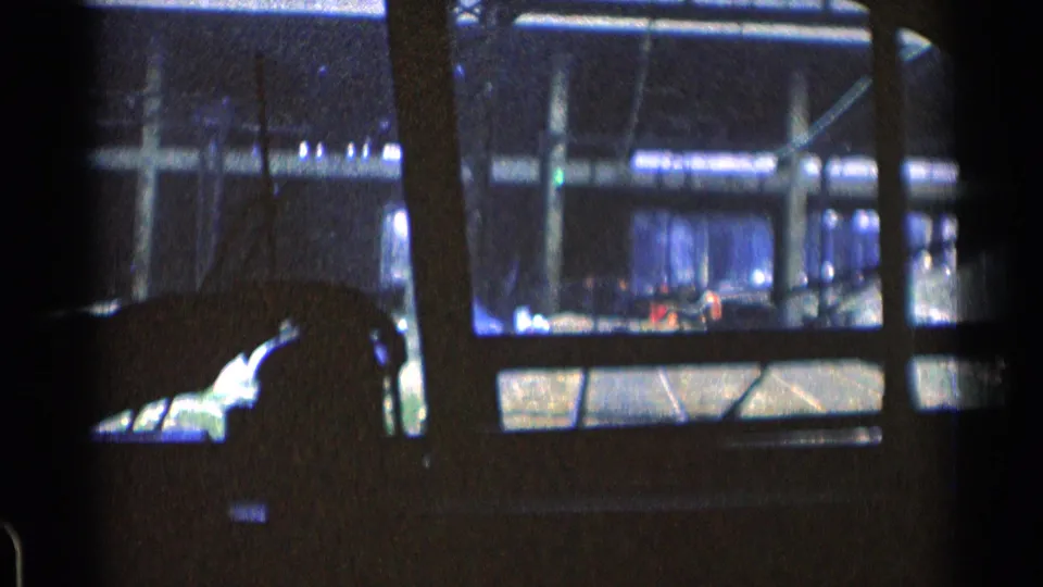 Blue-tinted 8mm view from a moving Chicago train or trolley, with window bars, railings, concrete structure, and a passing train-like form.