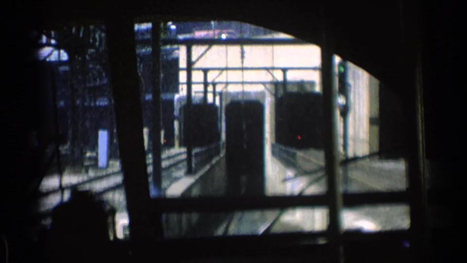Chicago 1976 8mm frame of rail tracks, a large arched structural opening, railings, and dark window silhouettes from inside transit.