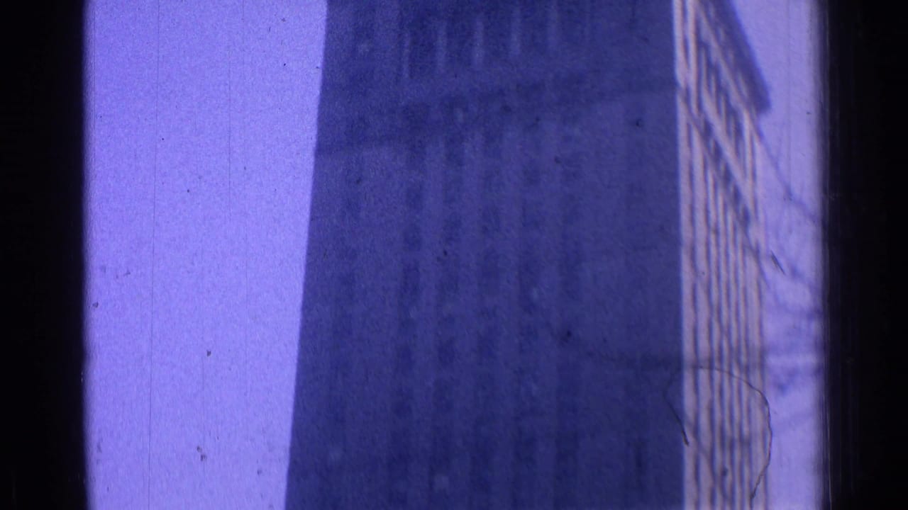 Tall building facade seen through a dark vertical frame with a purple film cast.