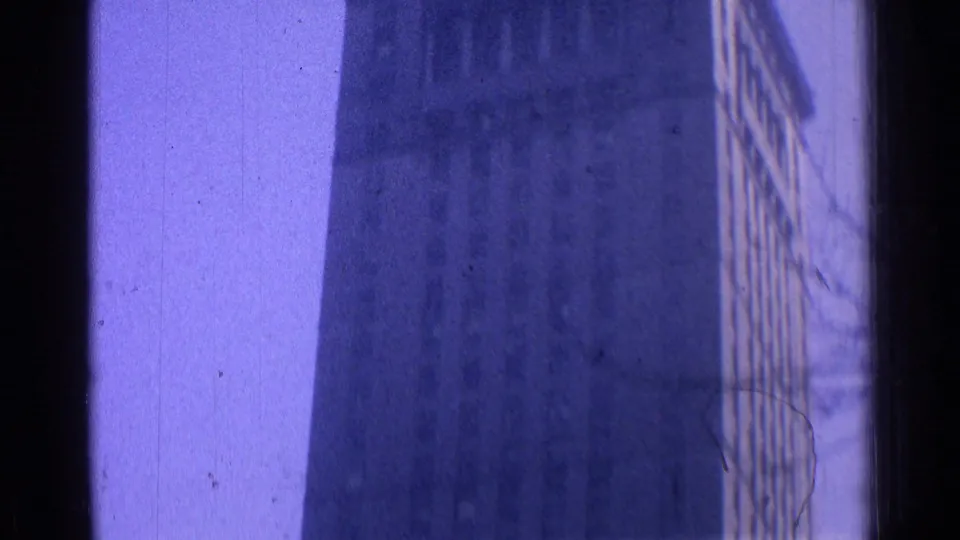1976 Chicago home-movie frame showing a tall windowed building facade partially obscured by a dark vertical edge and purple color shift.