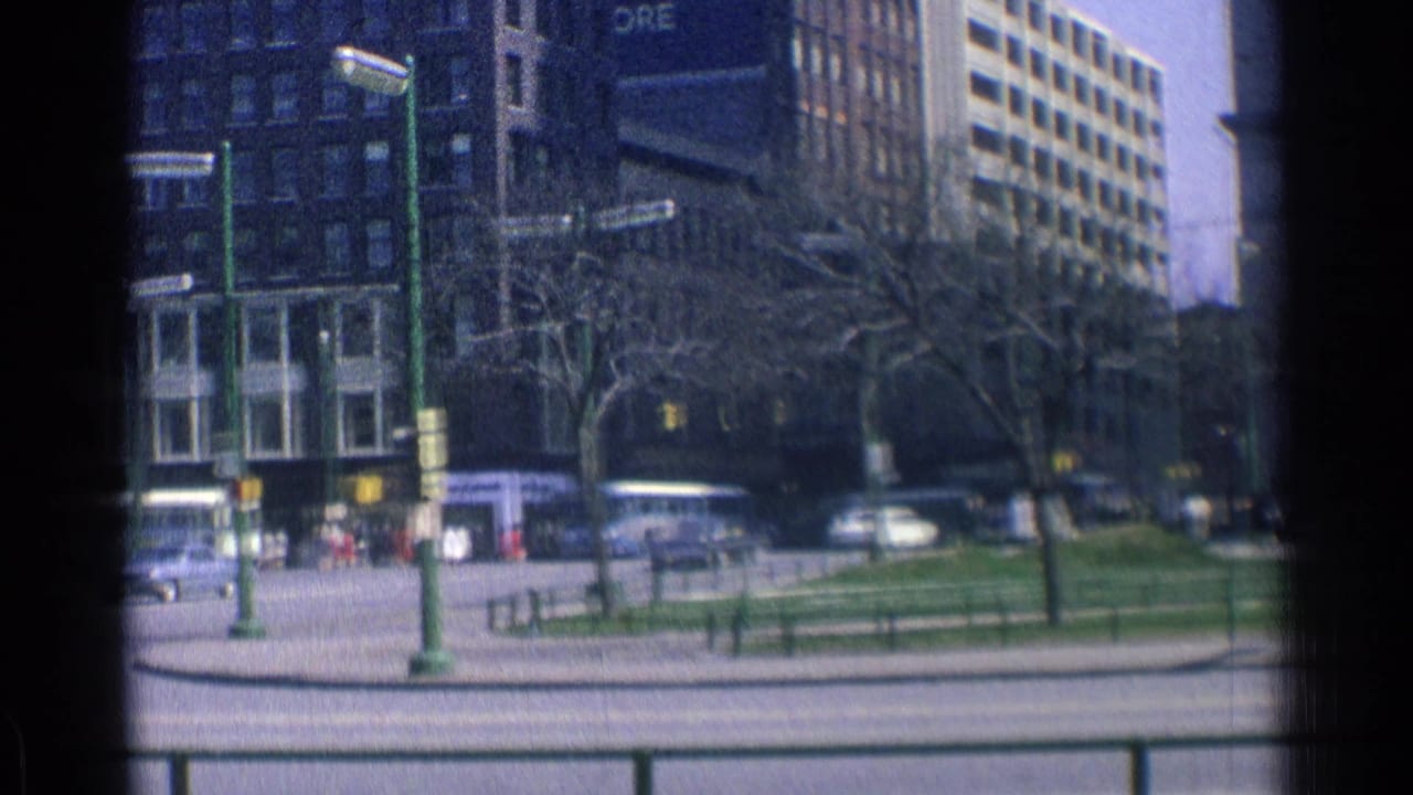 Downtown street with tall buildings, trees, traffic, and green street poles.
