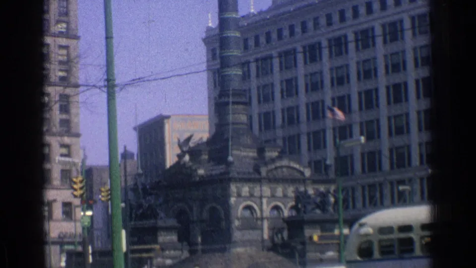 1976 downtown Chicago frame showing a stone tower, nearby buildings, traffic signals, and the front of a bus at the street edge.