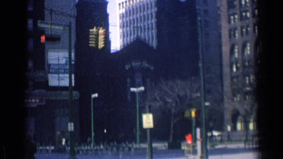 1976 Chicago street frame showing a church-like facade, tall office buildings, traffic signals, signs, and a few distant pedestrians.