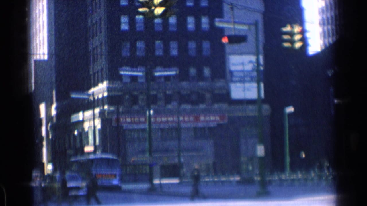 Downtown street corner with tall buildings, storefront signage, pedestrians, and a bus or truck at the curb.