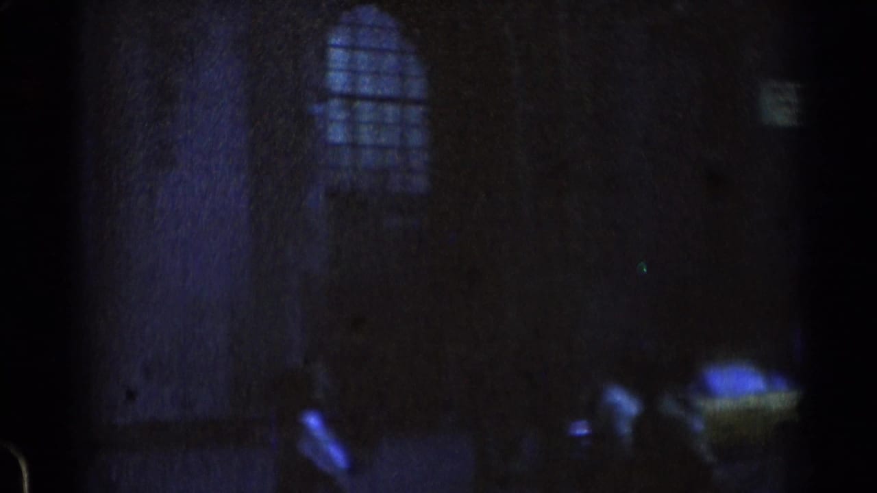 Dark opening frame from 1976 8mm Chicago rail footage, with a faint arched window shape and barely visible platform-side forms.