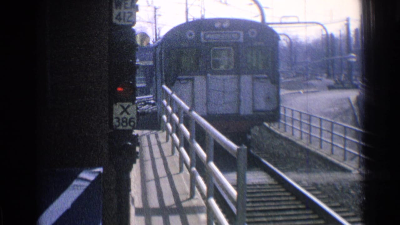 1976 Chicago 8mm frame showing a blue railcar approaching beside platform railings and a signal post marked WE 412 and X 386.