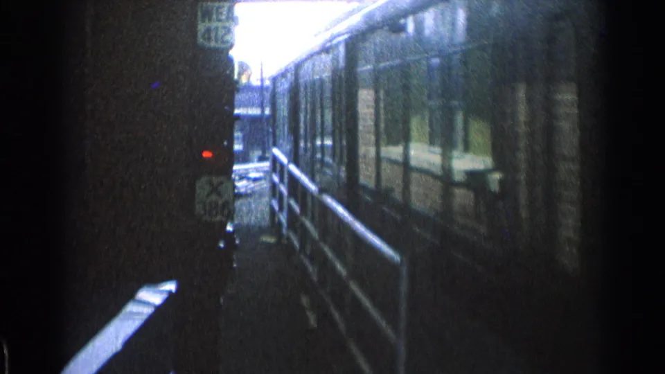Side view of the blue Chicago railcar passing close to the platform, with reflected windows, railings, and dark 8mm frame edges.