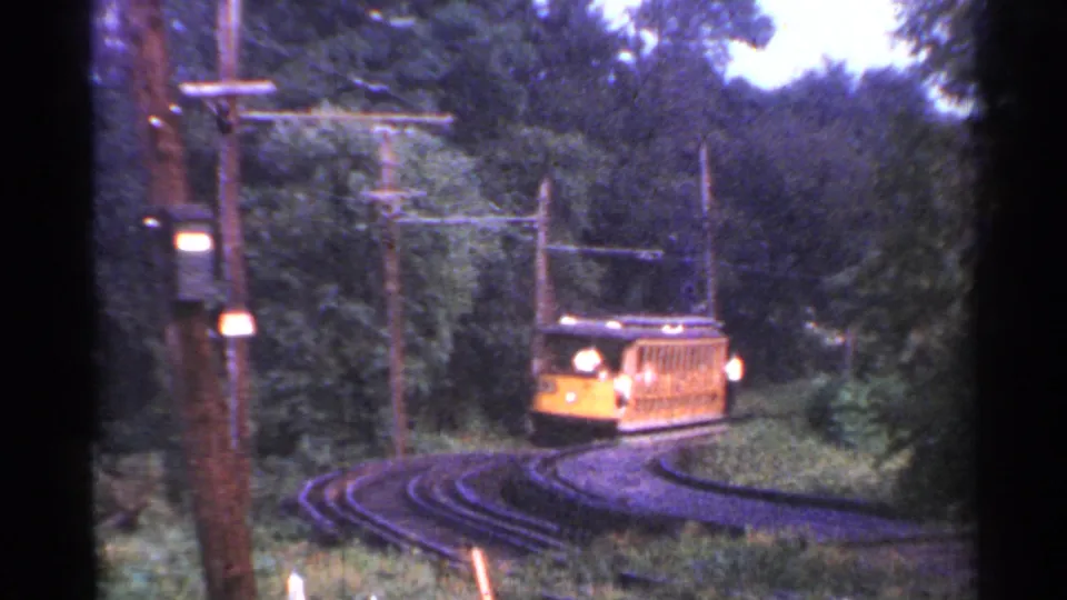 A yellow trolley approaches on the curved rail line, framed by trees, grass, poles and visible 8mm film edges.