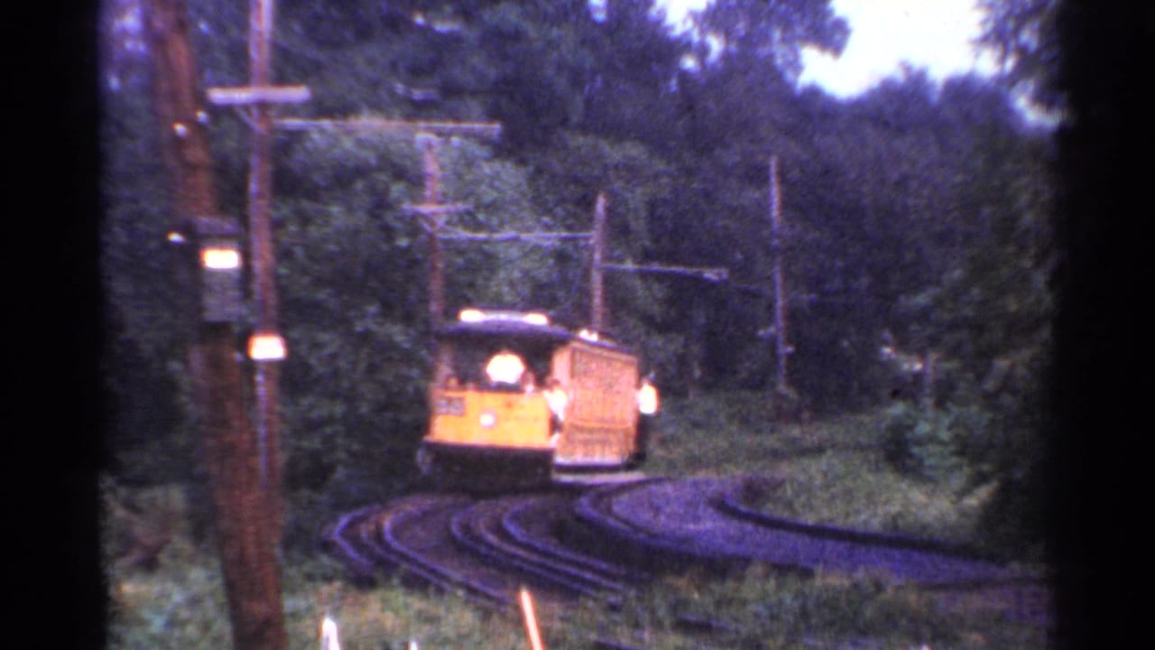 1953 Connecticut 8mm frame showing a yellow trolley rounding narrow rails through trees, with an operator visible at the front.