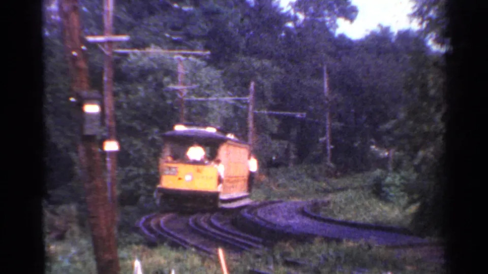 The trolley continues along the curve, framed by trees, rails, utility poles, and overhead wire supports in Connecticut footage from 1953.