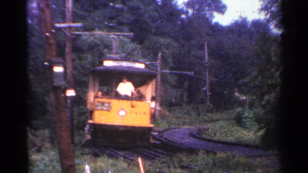 1953 Connecticut 8mm frame showing a yellow trolley approaching along rails through trees, with a conductor visible at the front.