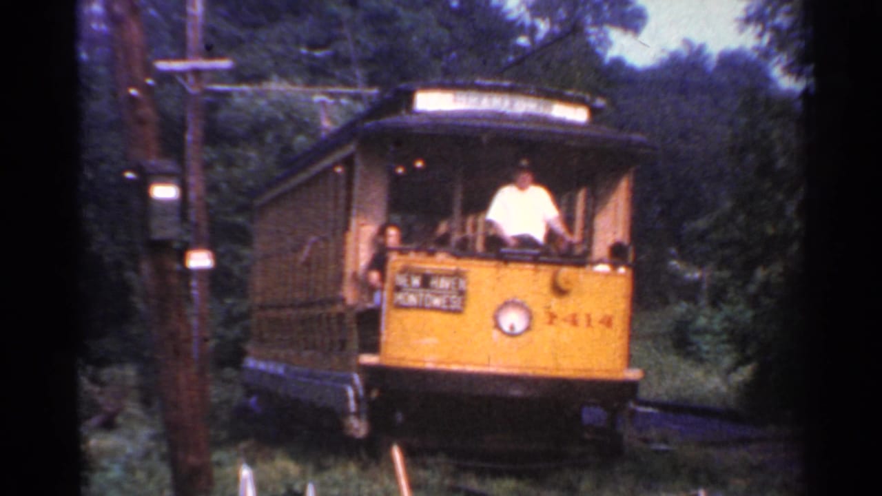 Yellow trolley car nears the camera with passengers aboard.