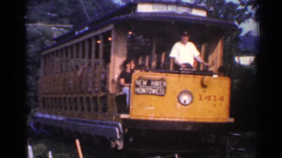Close view of the yellow trolley front and open side, with New Haven Montowese wording visible and the conductor standing at the controls.