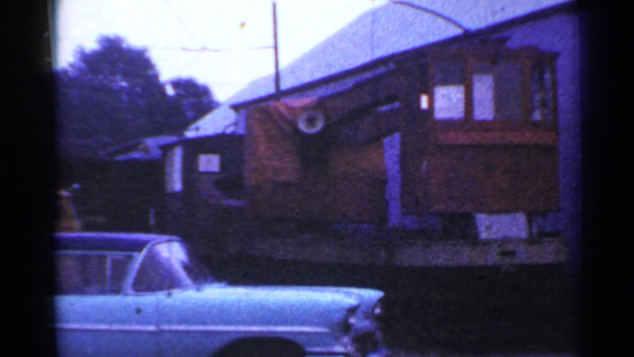 1953 Connecticut frame showing a pale blue mid-century sedan near exterior buildings and a small rail or trolley car in the background.