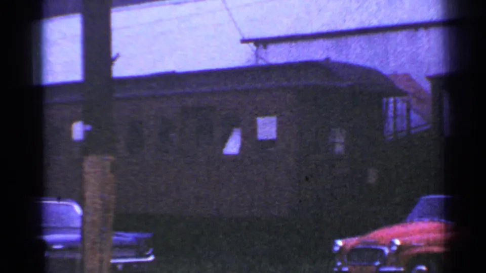 1953 Connecticut home-movie frame with a red convertible and another parked car beside a dark building exterior.