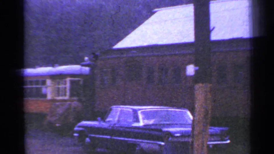 Connecticut 1953 frame showing a dark mid-century car in front of buildings, with a small rail or trolley car in the background.