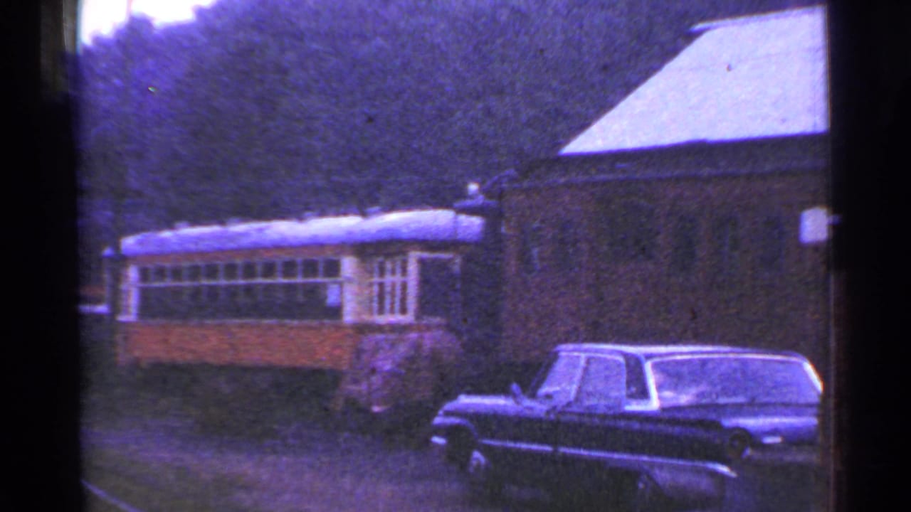 1953 Connecticut 8mm frame showing a yellow and gray passenger rail car, brick station building, trees, and a dark sedan.