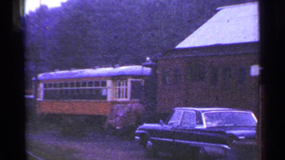 1953 Connecticut 8mm frame showing a yellow and gray passenger rail car, brick station building, trees, and a dark sedan.