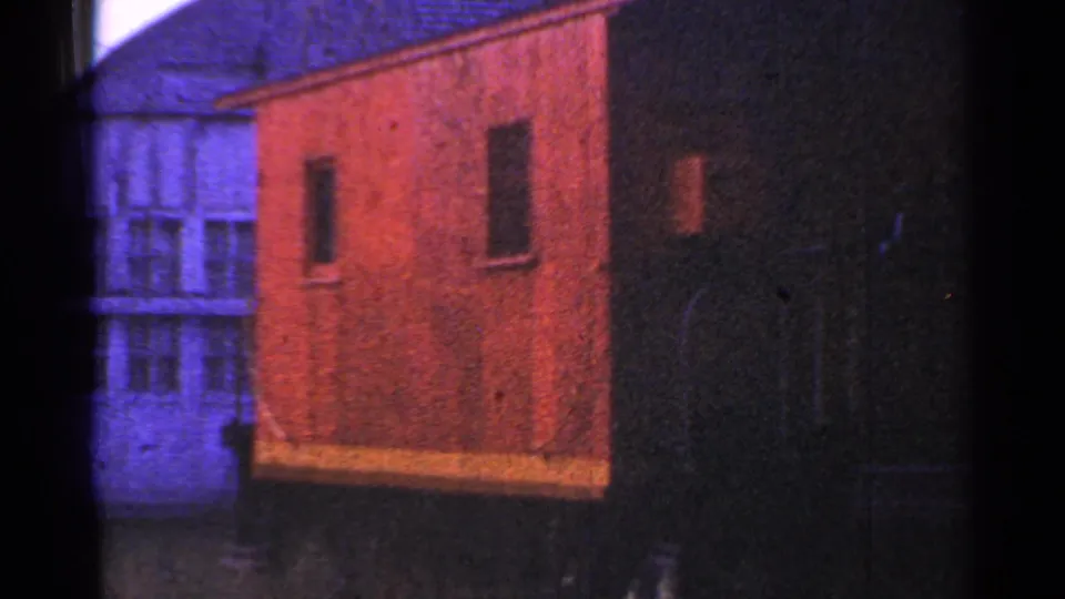 1953 Connecticut campsite frame with a red-orange shelter, dark neighboring structure, and pale building behind.
