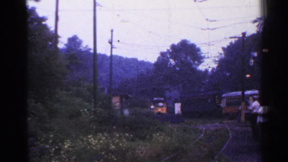 1953 Connecticut rail scene with a distant train, wooded curve, utility poles, and a person in light clothing near the tracks.