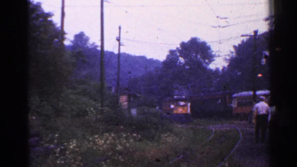 Wooded 1953 Connecticut rail view with an approaching train, nearby railcar, and a person walking along the trackside.
