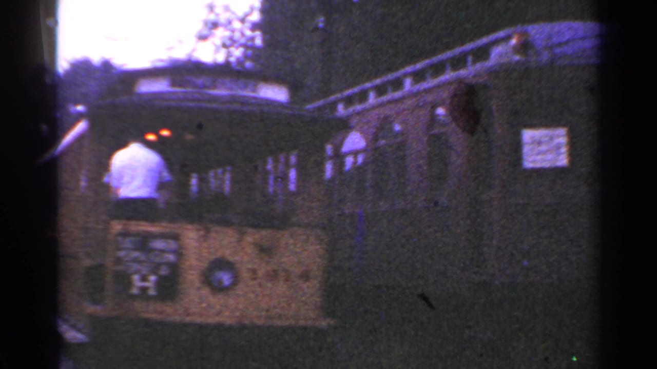 1953 Connecticut 8mm frame showing a person at the front of an open-sided trolley with arched windows beside a wooded area.