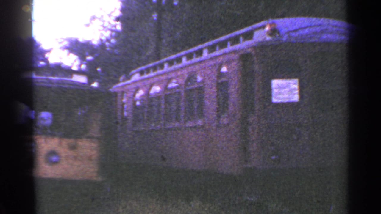 Side view of an open-sided trolley car with arched windows and a sign.