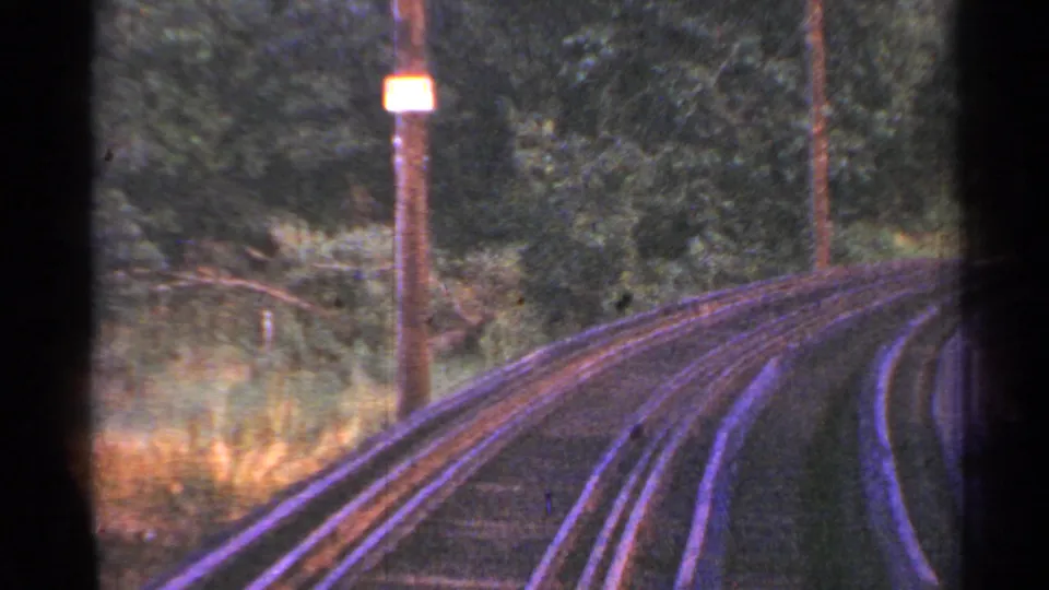 1953 Connecticut 8mm view down curving trolley rails bordered by grass, trees, a pole, and a small trackside sign.