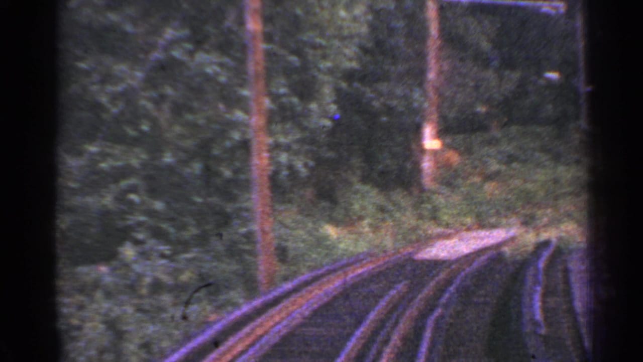 1953 Connecticut 8mm frame showing a forward train-ride view as rails curve through green woodland.