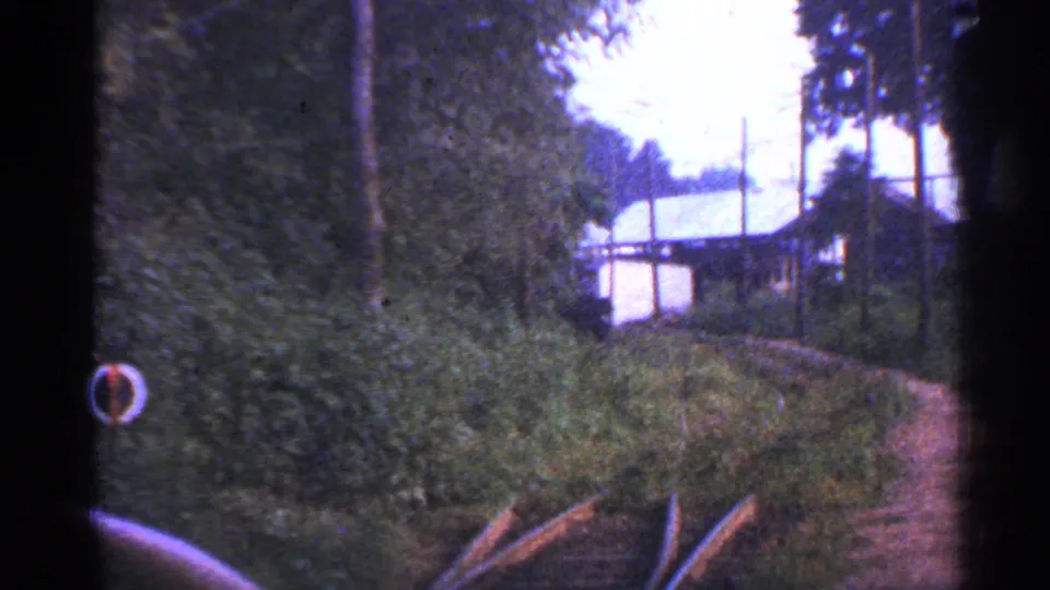 1953 Connecticut 8mm frame looking along overgrown tracks toward a small pale structure partly screened by trees.