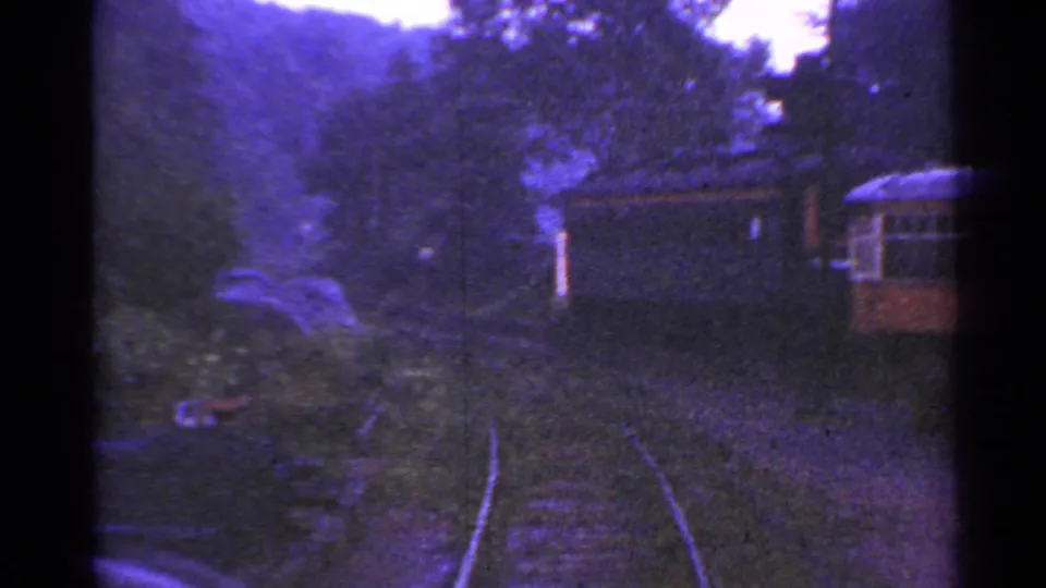 Aged 8mm view of Connecticut railroad tracks curving through greenery toward small rail vehicles or cars.