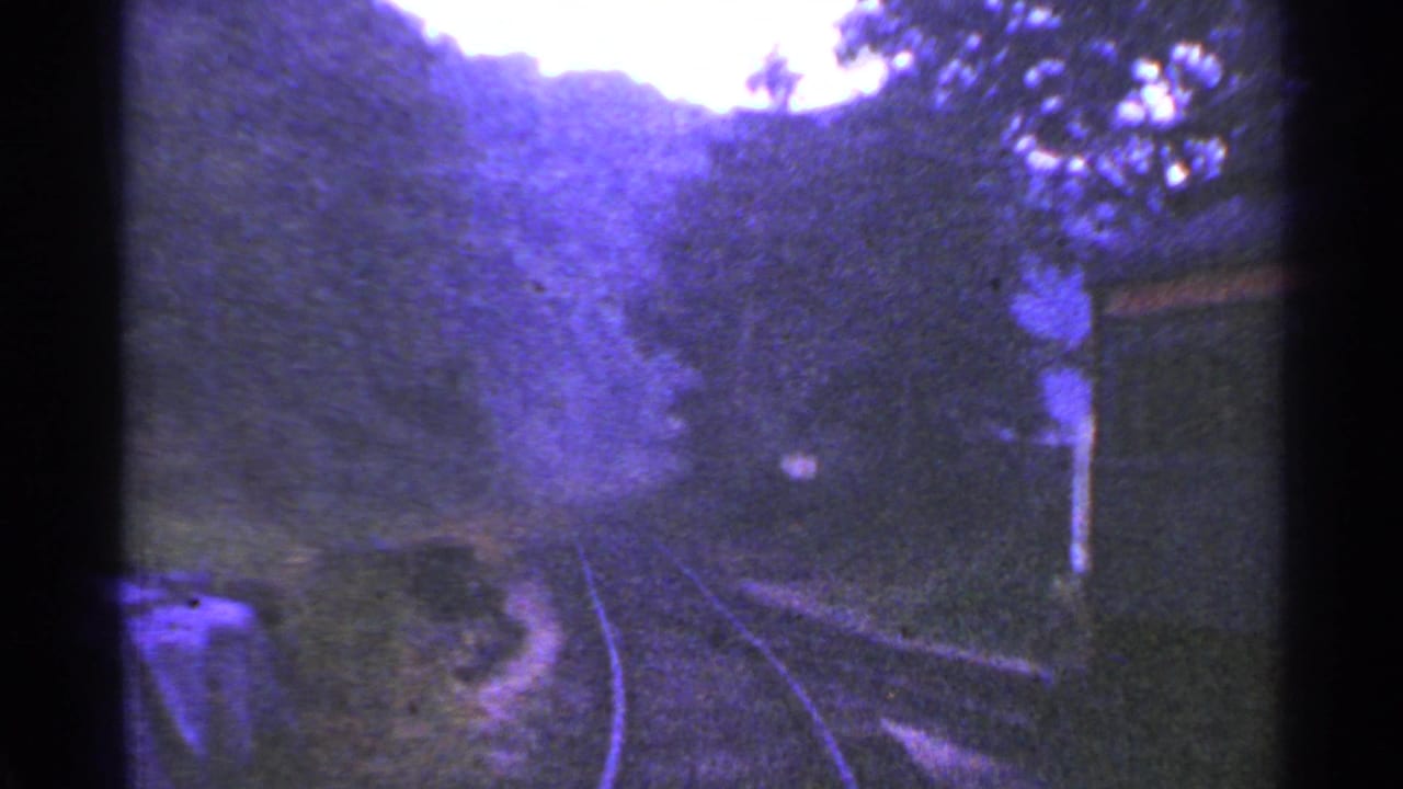 1953 Connecticut rail-view frame with curving tracks, dense trees, and a small structure passing on the right side of the train view.