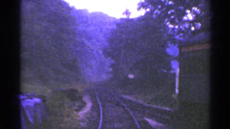 1953 Connecticut rail-view frame with curving tracks, dense trees, and a small structure passing on the right side of the train view.