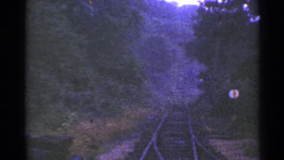 1953 Connecticut 8mm frame looking down rail tracks through dense foliage, with a round trackside sign visible near the right edge.