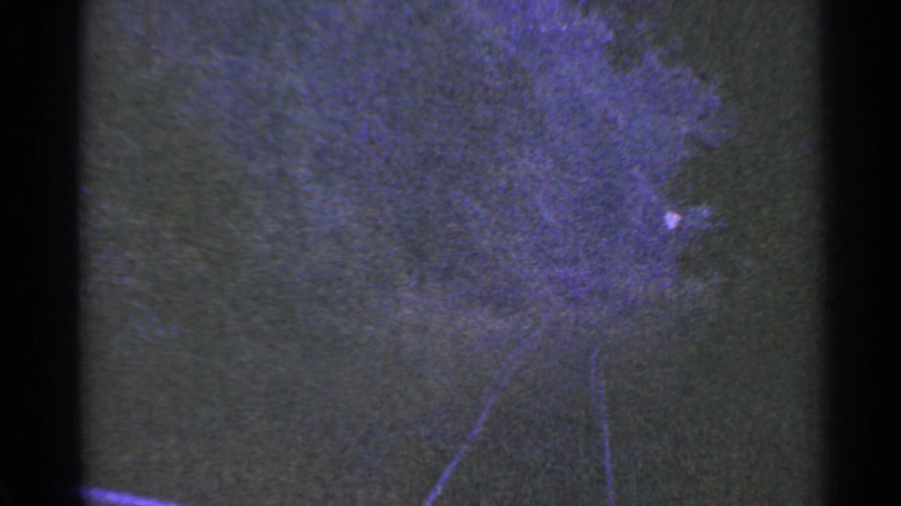 1953 Connecticut 8mm frame showing a dark textured surface with faint track-like lines, purple color shift, and visible film edges.