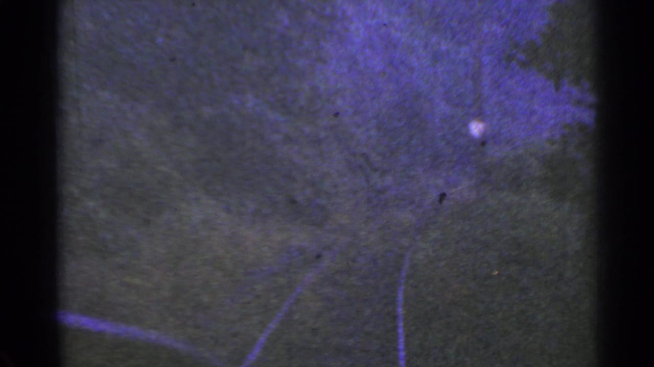 1953 Connecticut home-movie frame with a dark textured surface, faint curving lines, purple-tinted exposure, and film gate edges.