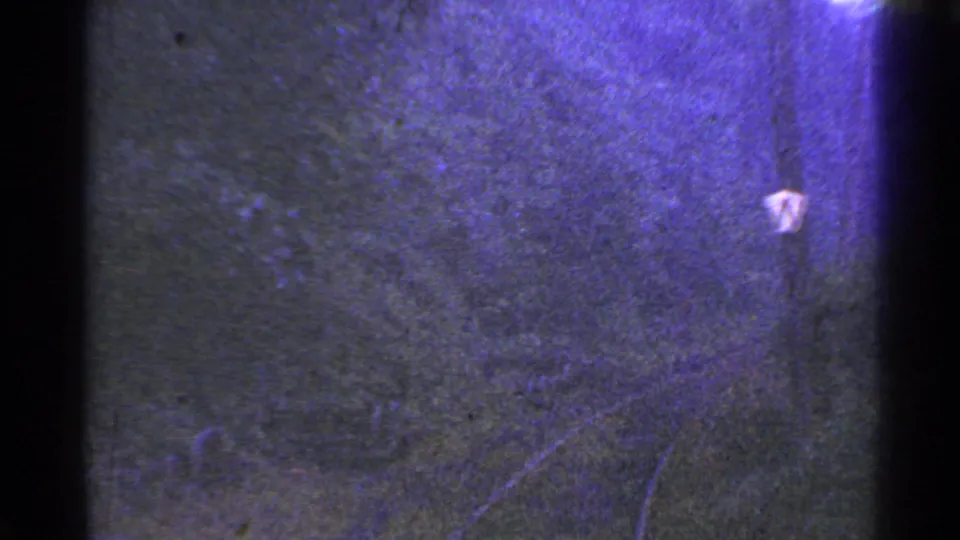 1953 Connecticut 8mm frame showing a small pale marker or sign against a dark textured surface with grain and purple color shift.