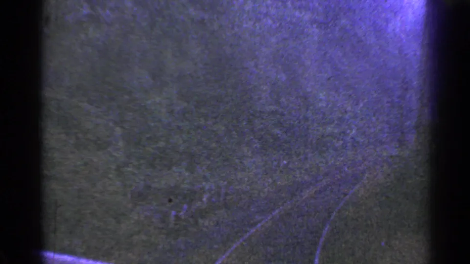 1953 Connecticut home-movie frame with dark textured surface, faint curved lines, purple-blue cast, and visible 8mm scan texture.