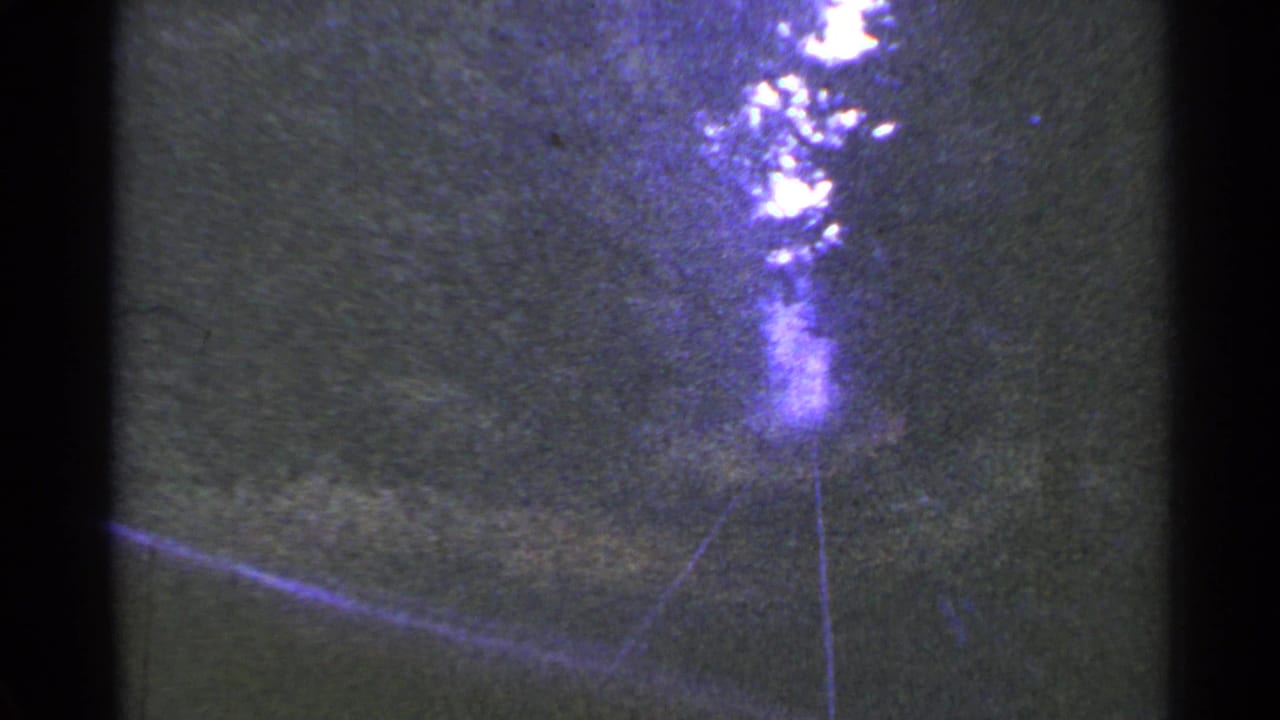 Rail tracks angle through trees toward a bright opening in a grainy frame.