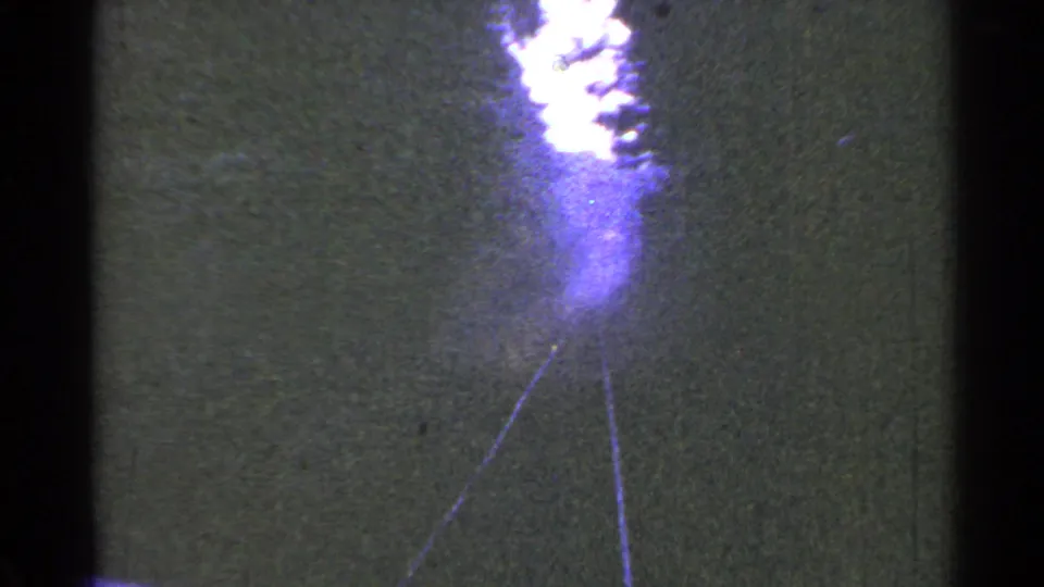 A 1953 home-movie frame shows the train-front perspective on rails running through trees, with strong exposure bloom at the top center.