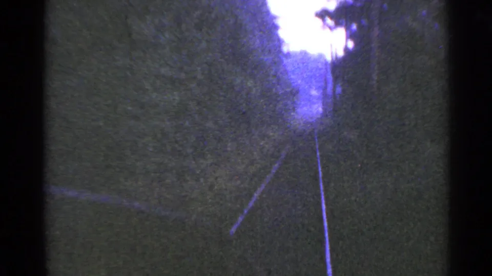 Final 8mm frame from the Connecticut rail POV shows tracks leading into dense trees and a bright overexposed area near the distance.