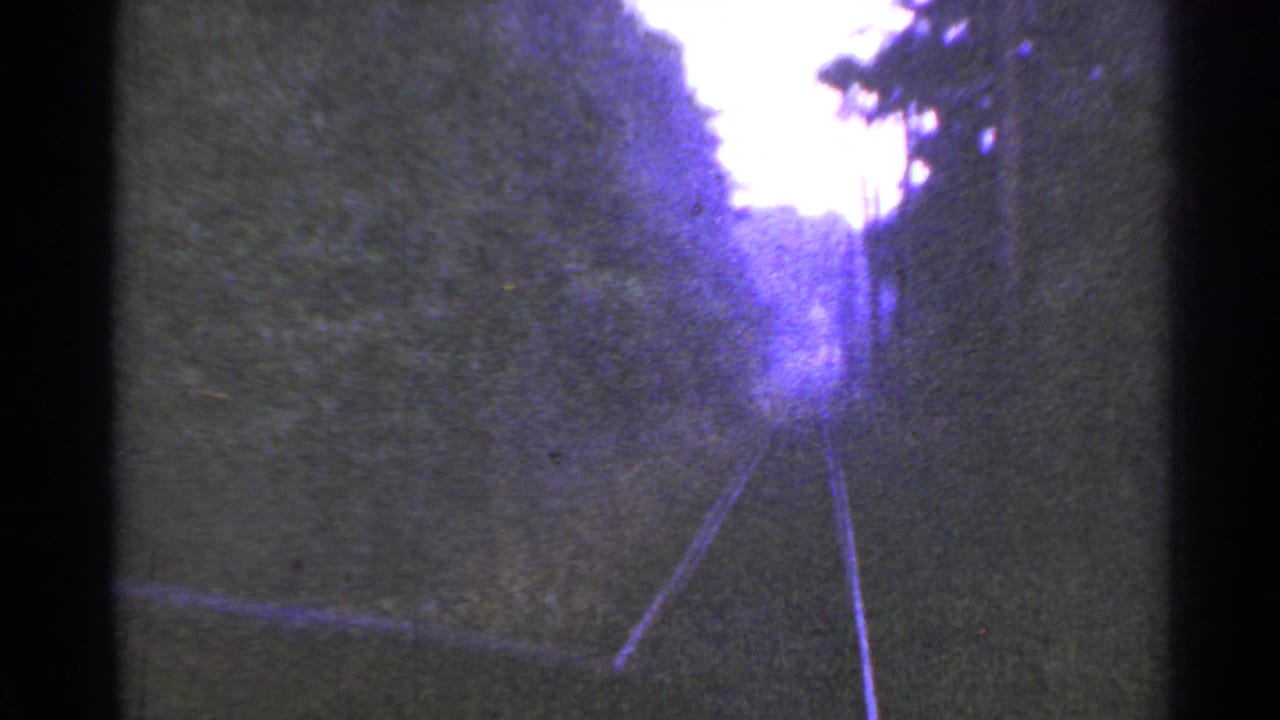 1953 Connecticut 8mm view looking down rural rail tracks between wooded embankments and a pale overexposed sky.