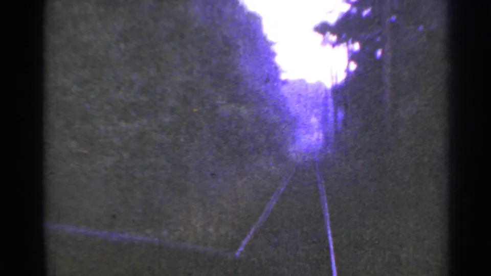 1953 Connecticut 8mm view looking down rural rail tracks between wooded embankments and a pale overexposed sky.