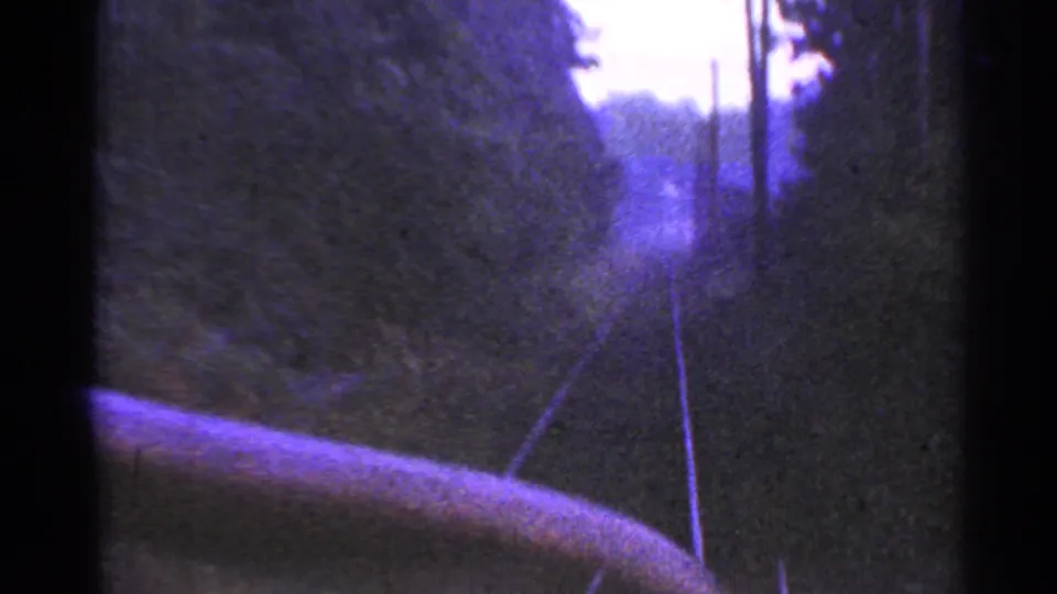 Moving 8mm passenger view down rural Connecticut tracks, with trees on both sides and a blurred foreground rail or vehicle edge.