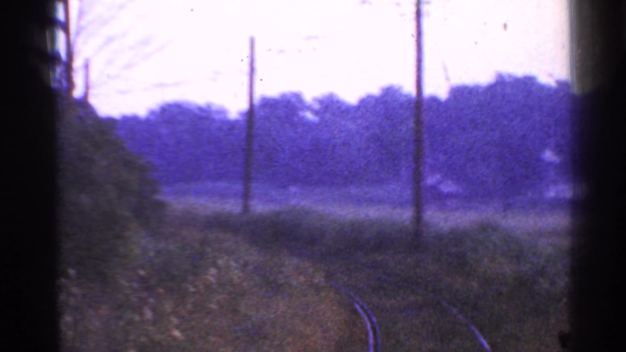 Moving-train POV in rural Connecticut, with curving rails, telephone poles, grass, and a dark vertical film edge.