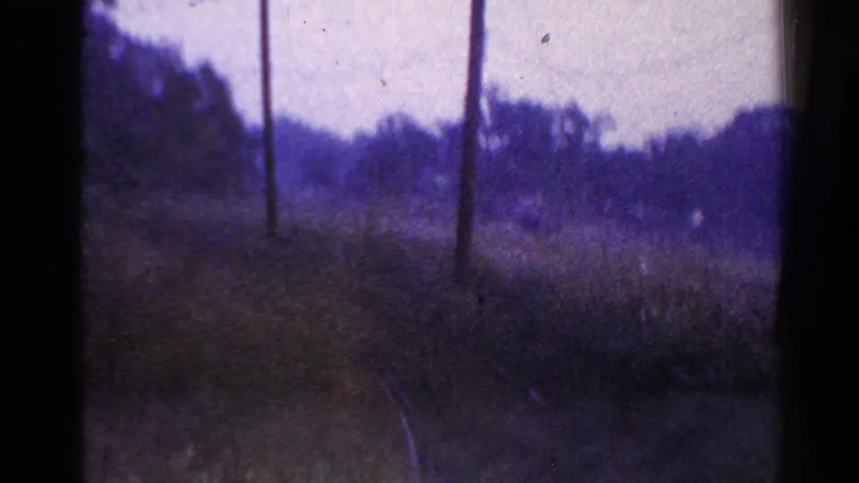 End frame of a 1953 Connecticut train POV showing curving track, pole line, grass, trees, and heavy 8mm texture.